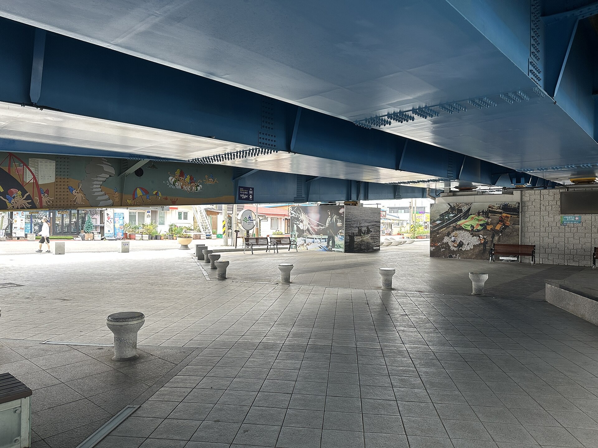 Public seating and painted surfaces beneath a bridge in Abai Village