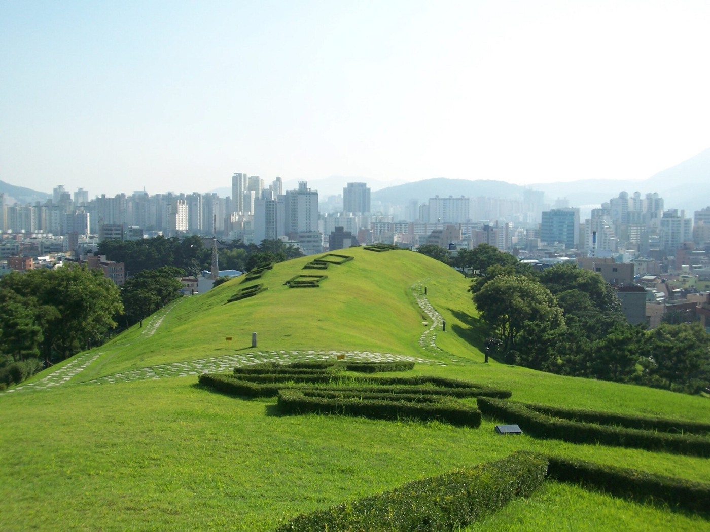 Excavated burial outlines against the modern Dongnae cityscape